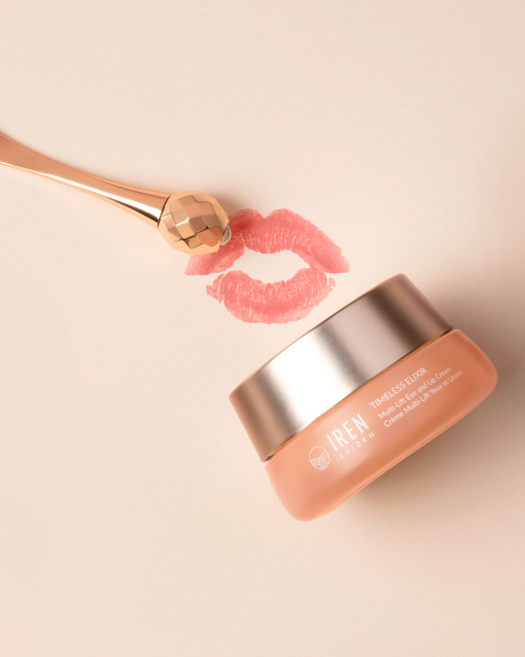 A jar of TIMELESS ELIXIR Multi-Lift Eye and Lip Cream by IREN Shizen, infused with Bakuchiol, sits next to a gold applicator and a lipstick kiss mark on a light beige background.