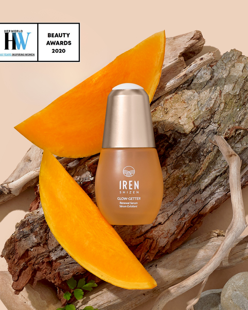 A bottle of IREN Shizen GLOW-GETTER Renewal Serum sits on wood with pumpkin slices, next to a "HW Beauty Awards 2020" badge on a beige background.