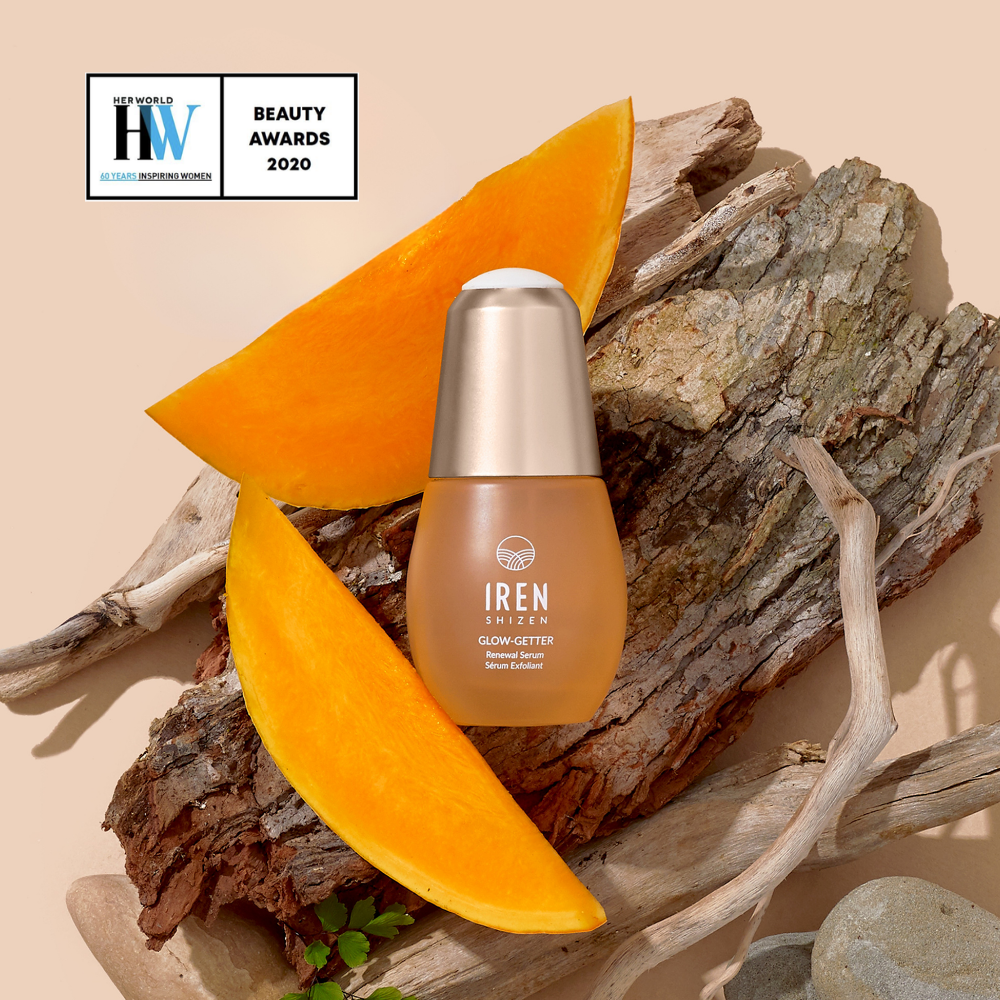A bottle of IREN Shizen GLOW-GETTER Renewal Serum sits on wood with pumpkin slices, next to a "HW Beauty Awards 2020" badge on a beige background.