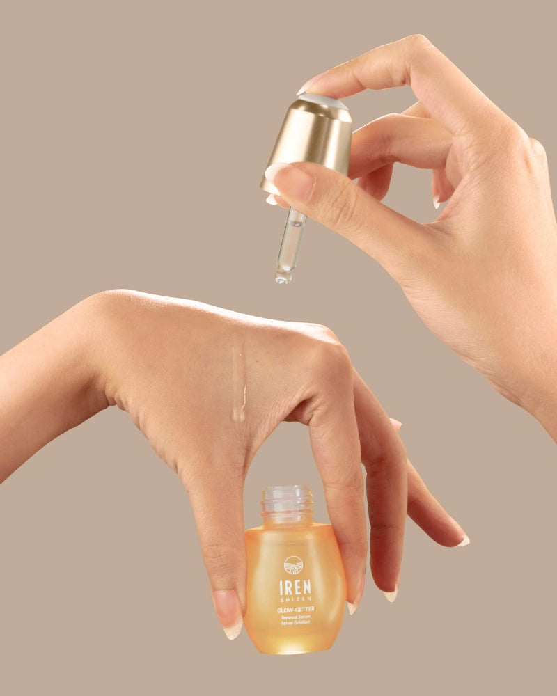 A hand holds a dropper above another hand, dispensing the GLOW-GETTER Renewal Serum by IREN Shizen—an exfoliating formula ideal for pore cleansing and targeting blackheads.