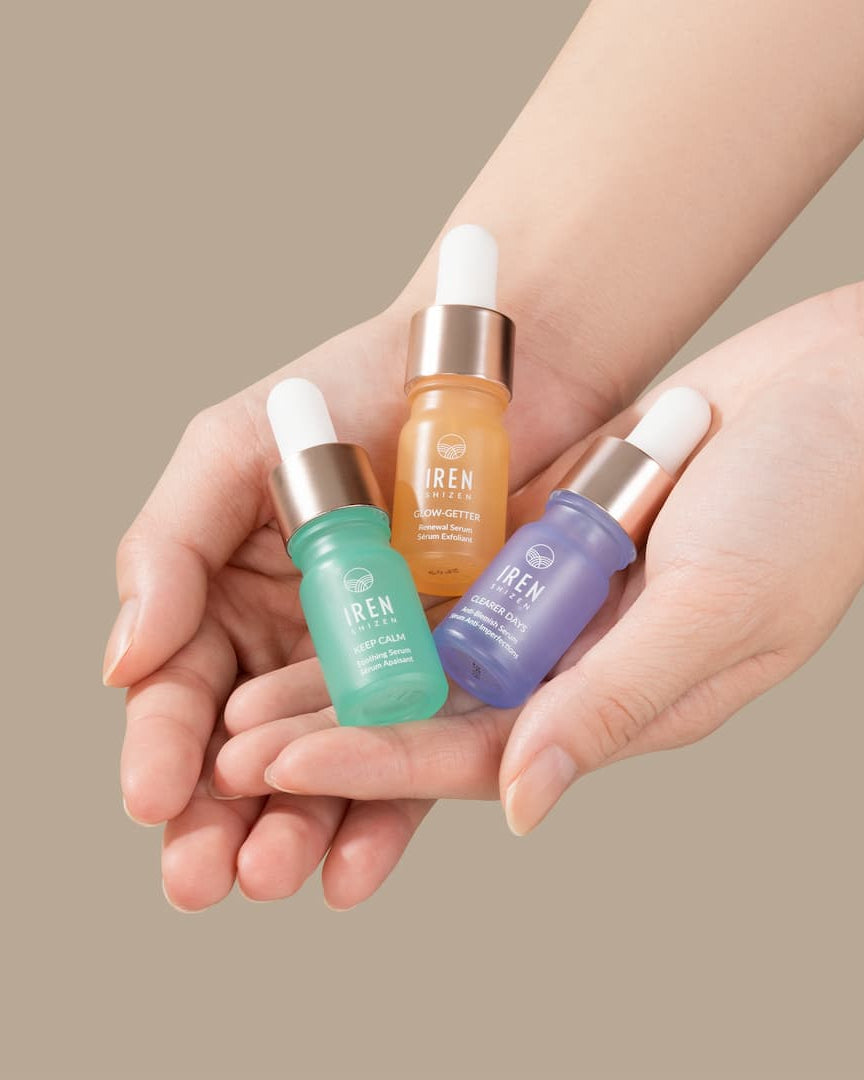 A woman's hands holding three different types of IREN Shizen's CLEAR UP Anti-Blemish Discovery Kit serums.