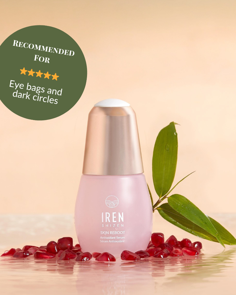 A bottle of SKIN REBOOT Antioxidant Serum by IREN Shizen is shown with pomegranate seeds, a green leaf, and a badge that recommends it for reducing dark circles and eye bags. #show-lang-en