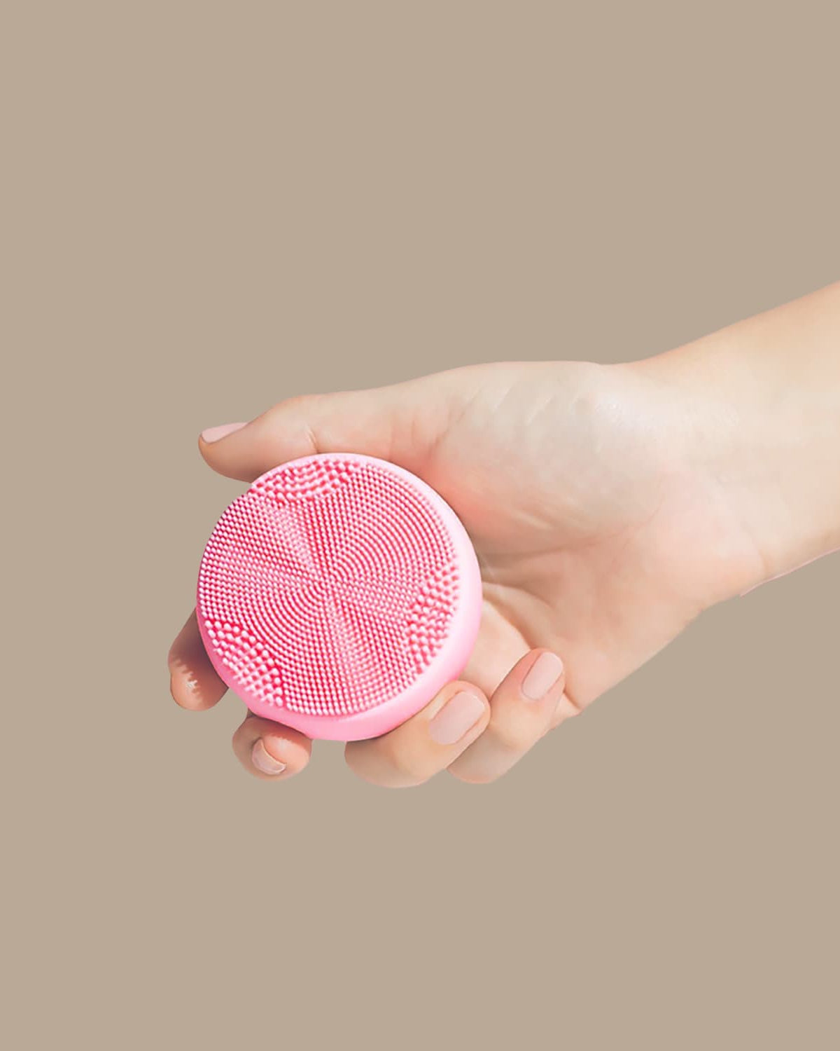 A hand holds the IREN Shizen SKIN GENIE PRO Hydration Set, a pink facial cleansing device with textured bristles and LED light therapy, against a plain beige background.