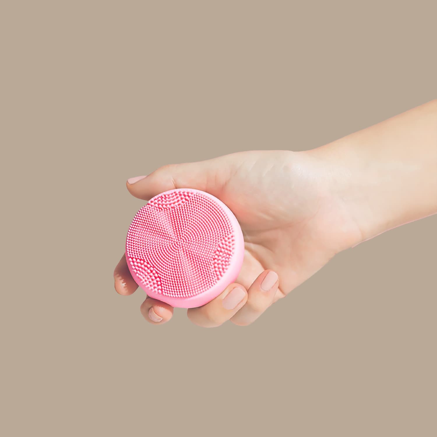 A hand holds the IREN Shizen SKIN GENIE PRO Hydration Set, a pink facial cleansing device with textured bristles and LED light therapy, against a plain beige background.