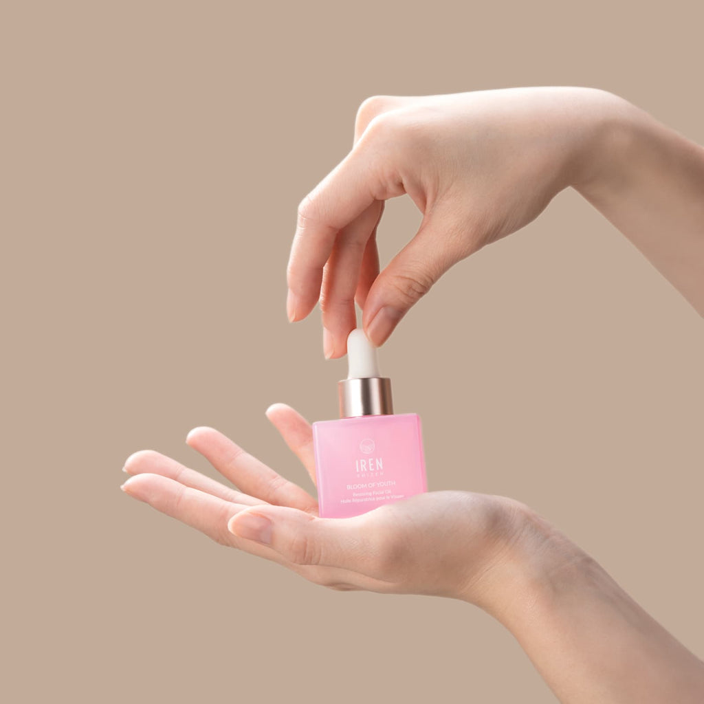 A woman's hand holding a firm BLOOM OF YOUTH Restoring Facial Oil bottle by IREN Shizen.