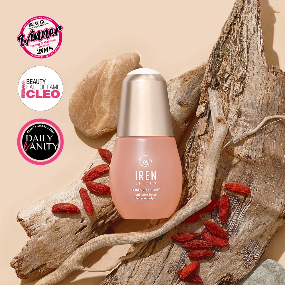 A bottle of IREN Shizen FOREVER YOUNG Anti-Aging Serum rests on driftwood with goji berries, framed by three award badges in the top left, emphasizing its anti-aging properties and collagen support. #all-groups