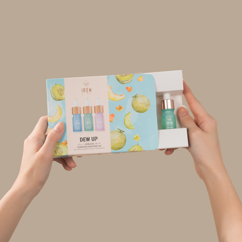 A hand holding a box with a bottle of juice and serum, providing hydration and protection with the DEW UP Hydrating Discovery Kit from IREN Shizen.
