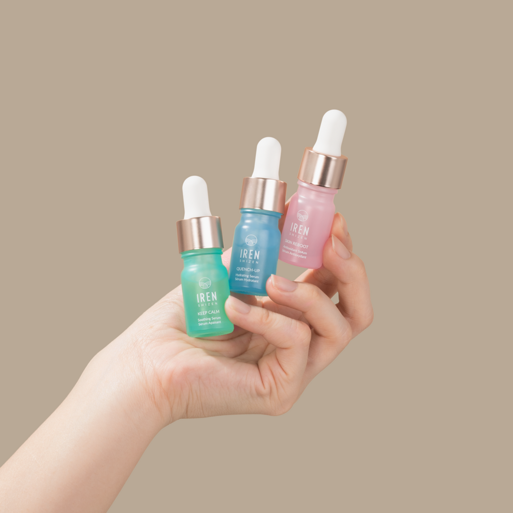 A woman's hand holding three different types of IREN Shizen DEW UP Facial Oil + Serums.