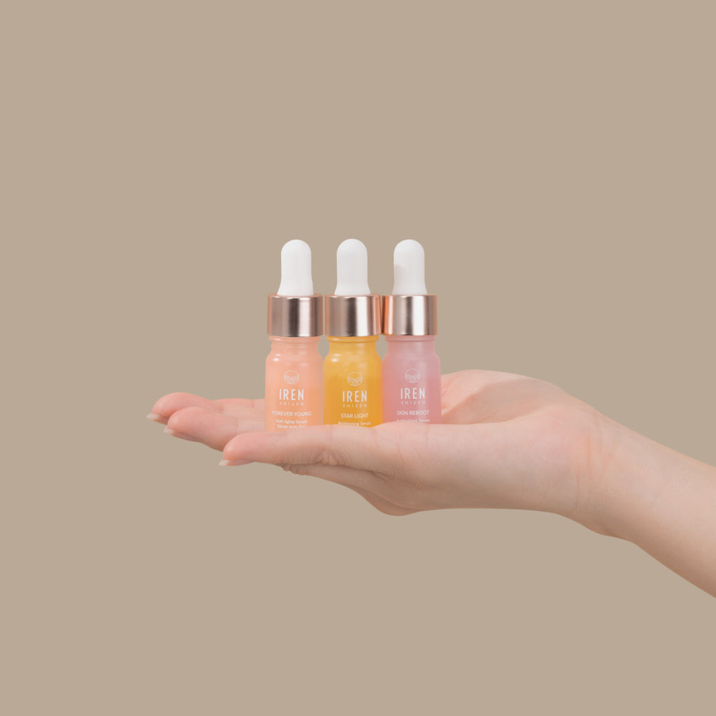A person's hand holding three different types of GLOW UP Facial Oil + Serums, including anti-aging and facial oil by IREN Shizen.