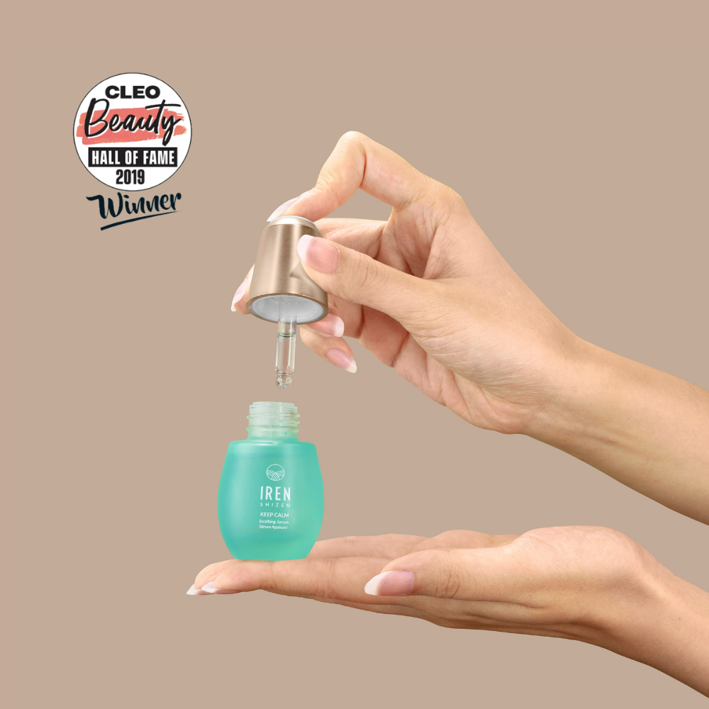 A hand holds a dropper over a blue KEEP CALM Soothing Serum bottle by IREN Shizen for sensitive skin, with another hand below. A "CLEO Beauty Hall of Fame 2019 Winner" badge is visible.