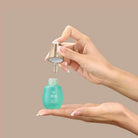 A person dispenses KEEP CALM Soothing Serum by IREN Shizen from a dropper bottle onto their palm against a plain beige background.