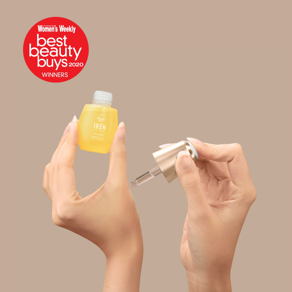 A person holds an open STAR LIGHT Brightening Serum bottle and dropper by IREN Shizen. A red badge reads "Women's Weekly Best Beauty Buys 2020 WINNERS," highlighting its dark spot and hyperpigmentation benefits.