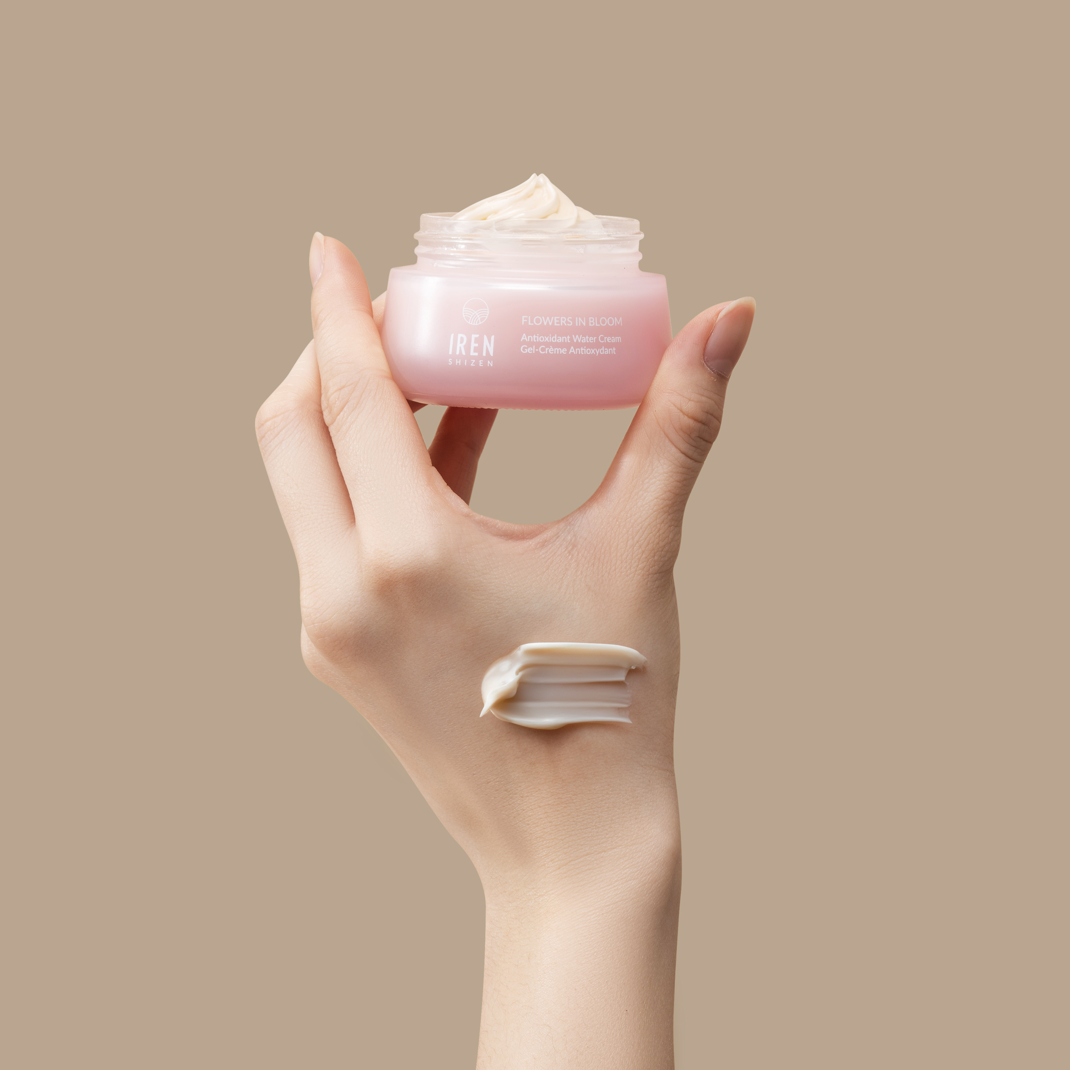 A hand holding an open jar of IREN Shizen&#39;s MOISTURE SANDWICH Skincare Kit with some product on the fingers against a neutral background.