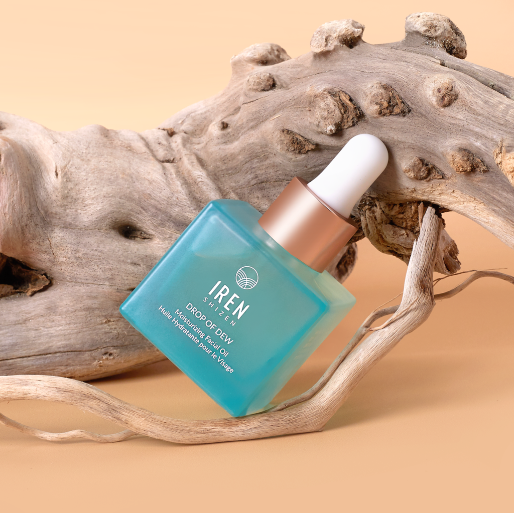 A bottle of Japanese customized skincare, DROP OF DEW Moisturizing Facial Oil, sitting on a piece of driftwood.