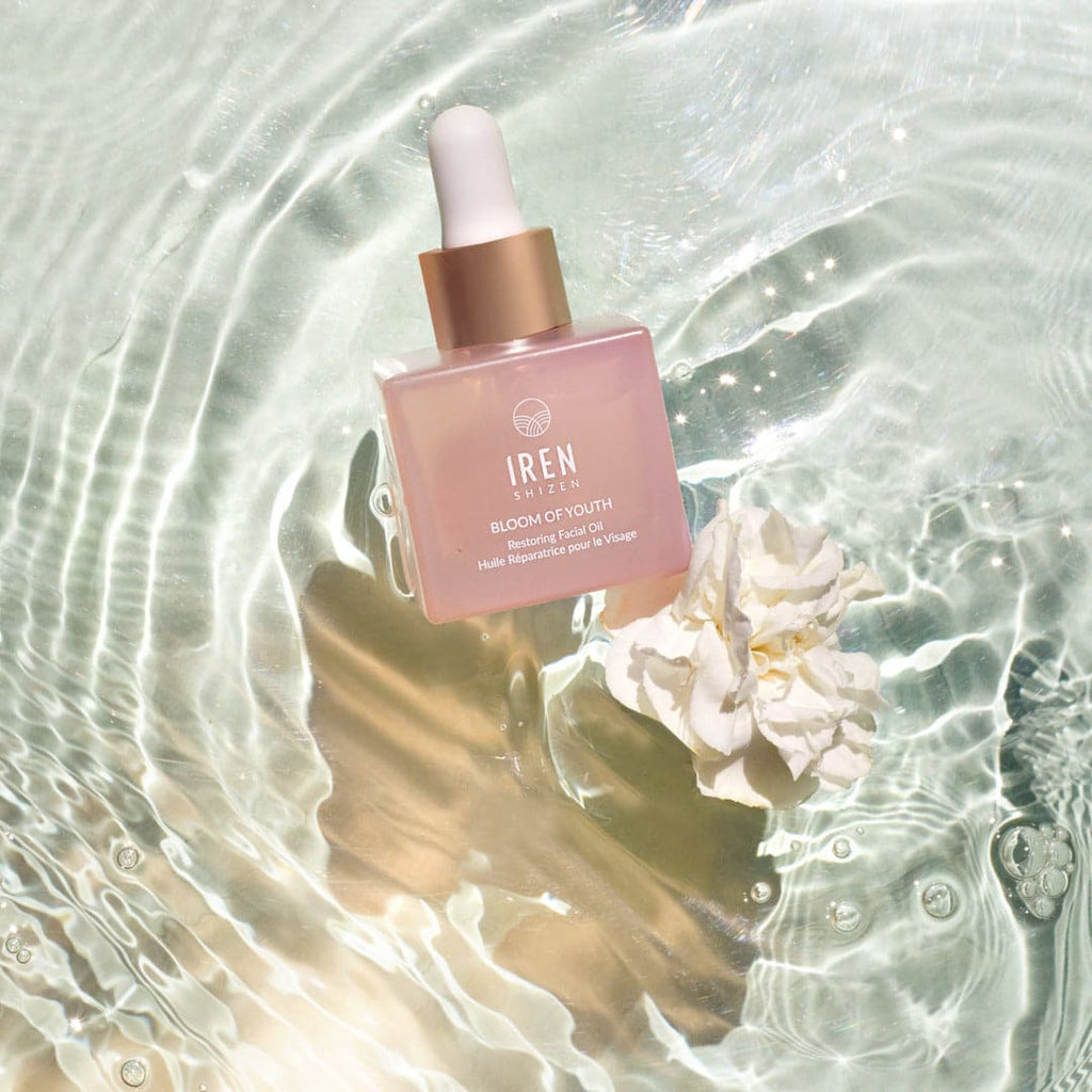 A bottle of customized BLOOM OF YOUTH Restoring Facial Oil by IREN Shizen sitting on top of water.