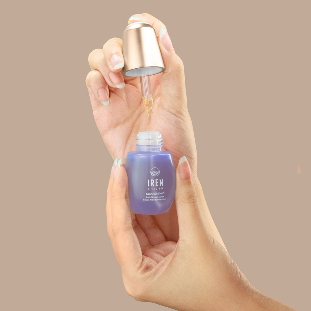 A hand holding a customized bottle of the IREN Shizen CLEAR UP Anti-Blemish Set.