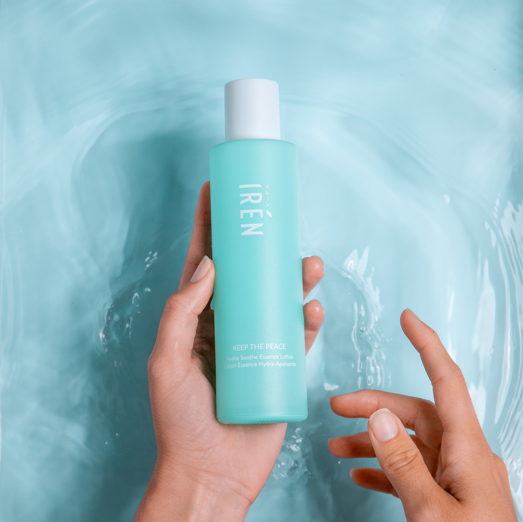 A woman's hand holding a bottle of customized IREN Shizen KEEP THE PEACE Hydra-Soothe Essence Lotion in the water.