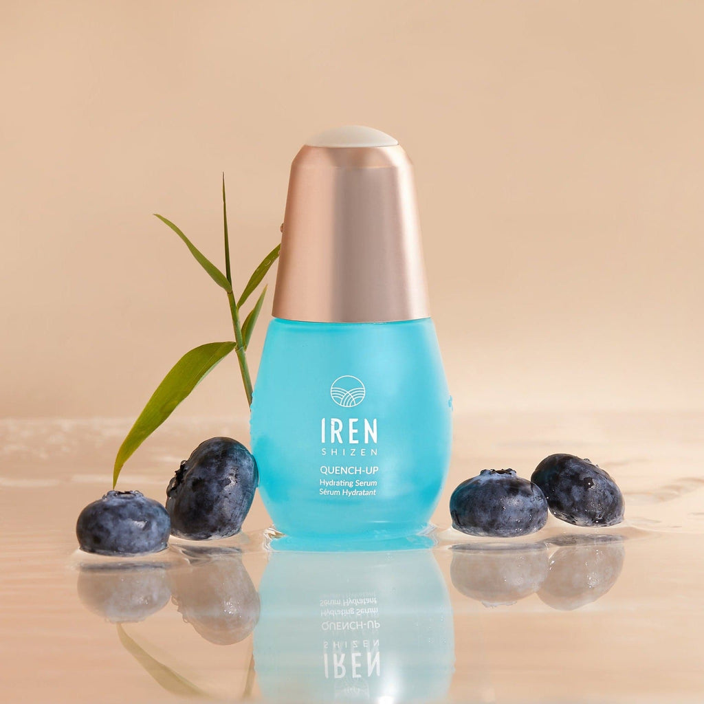 A bottle of custom Japanese skincare, IREN Shizen QUENCH-UP Hydrating Serum, next to some blueberries.