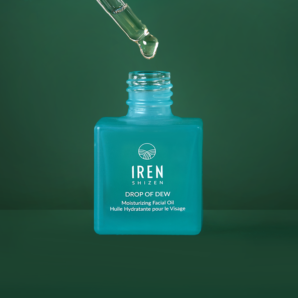 A bottle of custom DROP OF DEW Moisturizing Facial Oil by IREN Shizen on a green background.